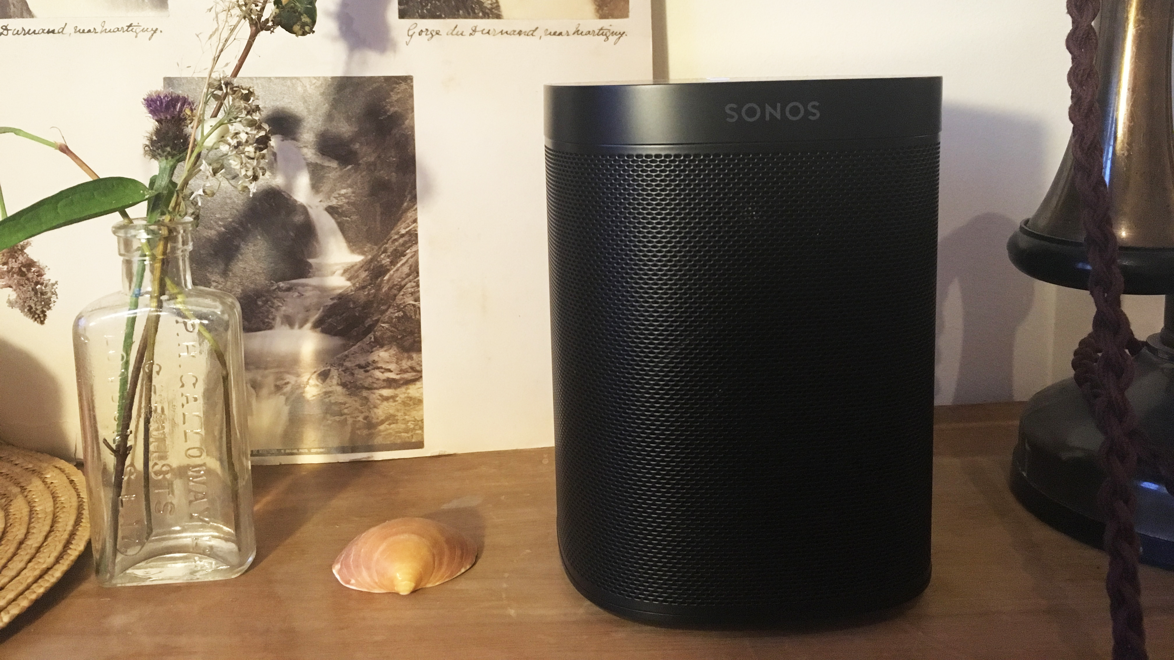 Speaker pintar Sonos One berwarna hitam di rak kayu