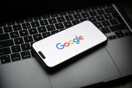 The Google logo displayed on a smartphone that's sitting on top of a laptop.