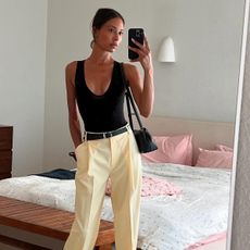 Tylynn wears a black tank, yellow trousers, and a black belt.