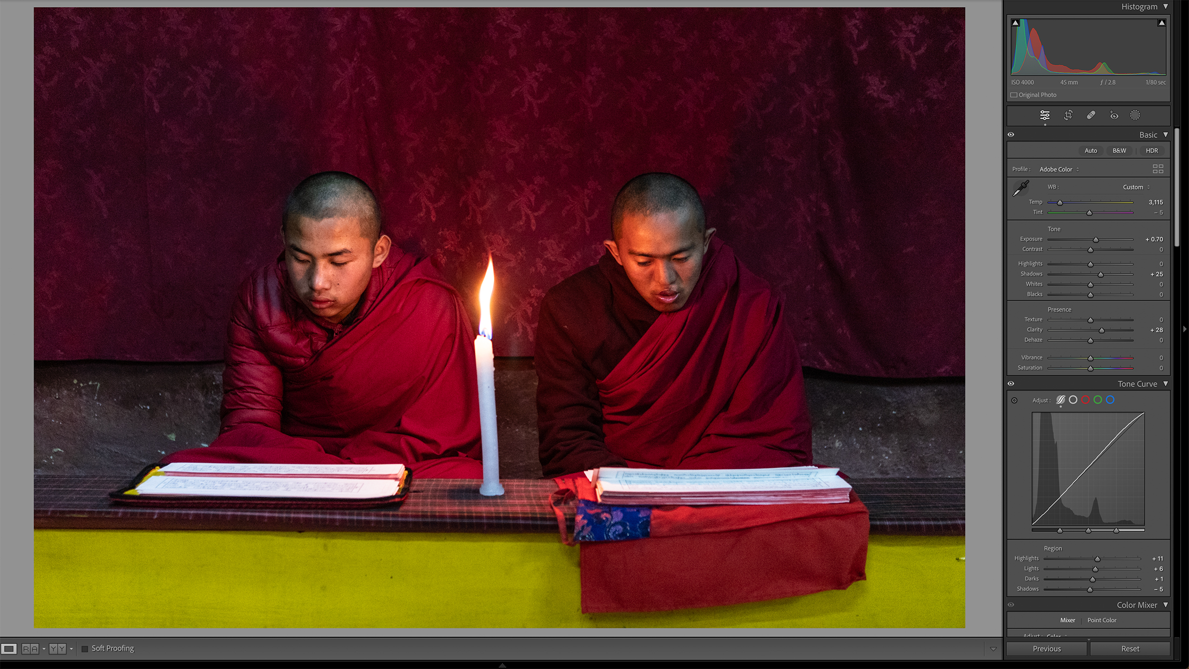 Two individuals in maroon robes are seated side by side, reading by candlelight. The dim setting conveys a calm and meditative atmosphere
