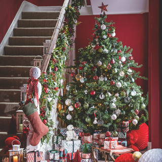 A Christmas tree in a home hallway, decorated with red and white tree decorations, and presents heaped up underneath.