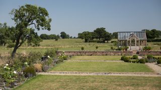 large garden with stone edging around lawns with greenhouse