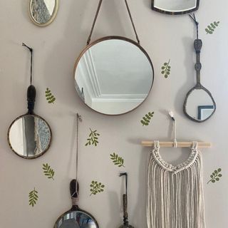 White wall with green plant stickers next to hanging mirror and macramé décor