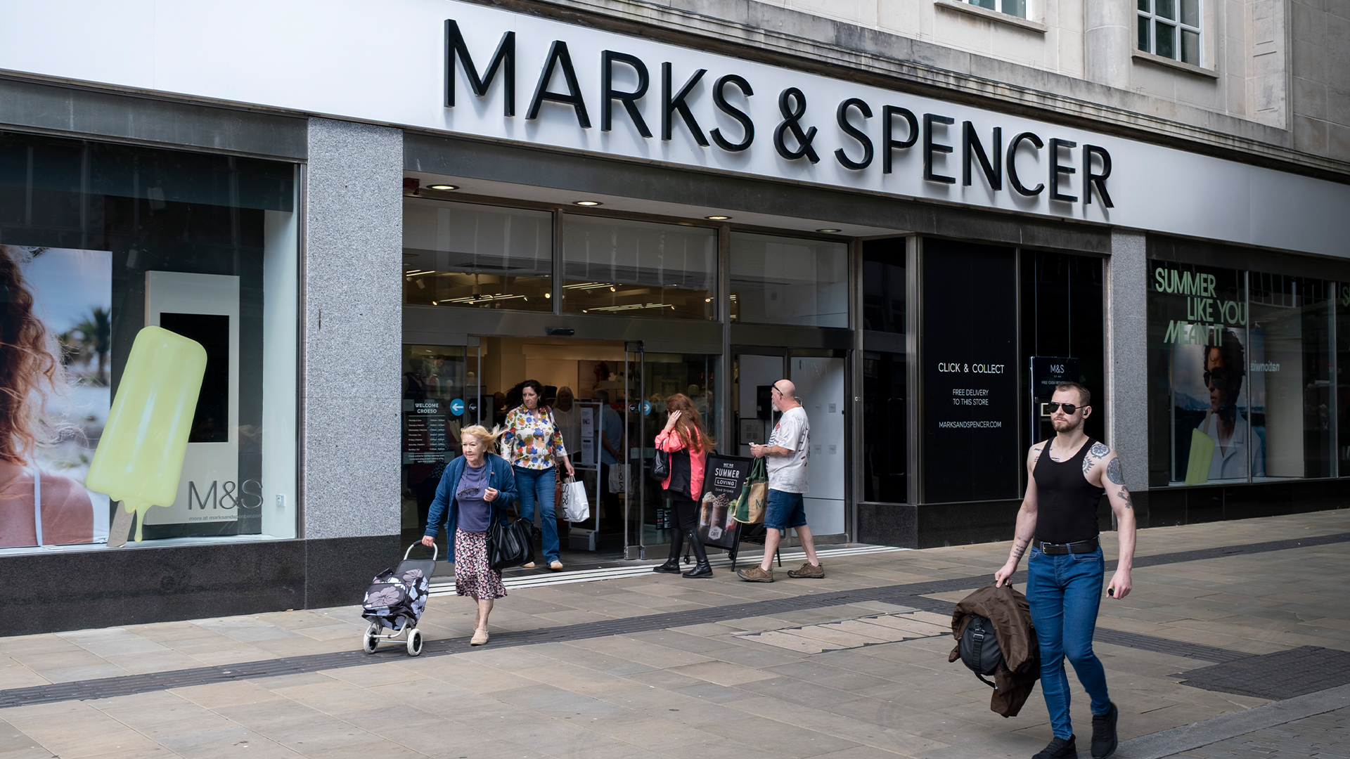 Pedestrians walking by an M&S store front in Swansea city center. 
