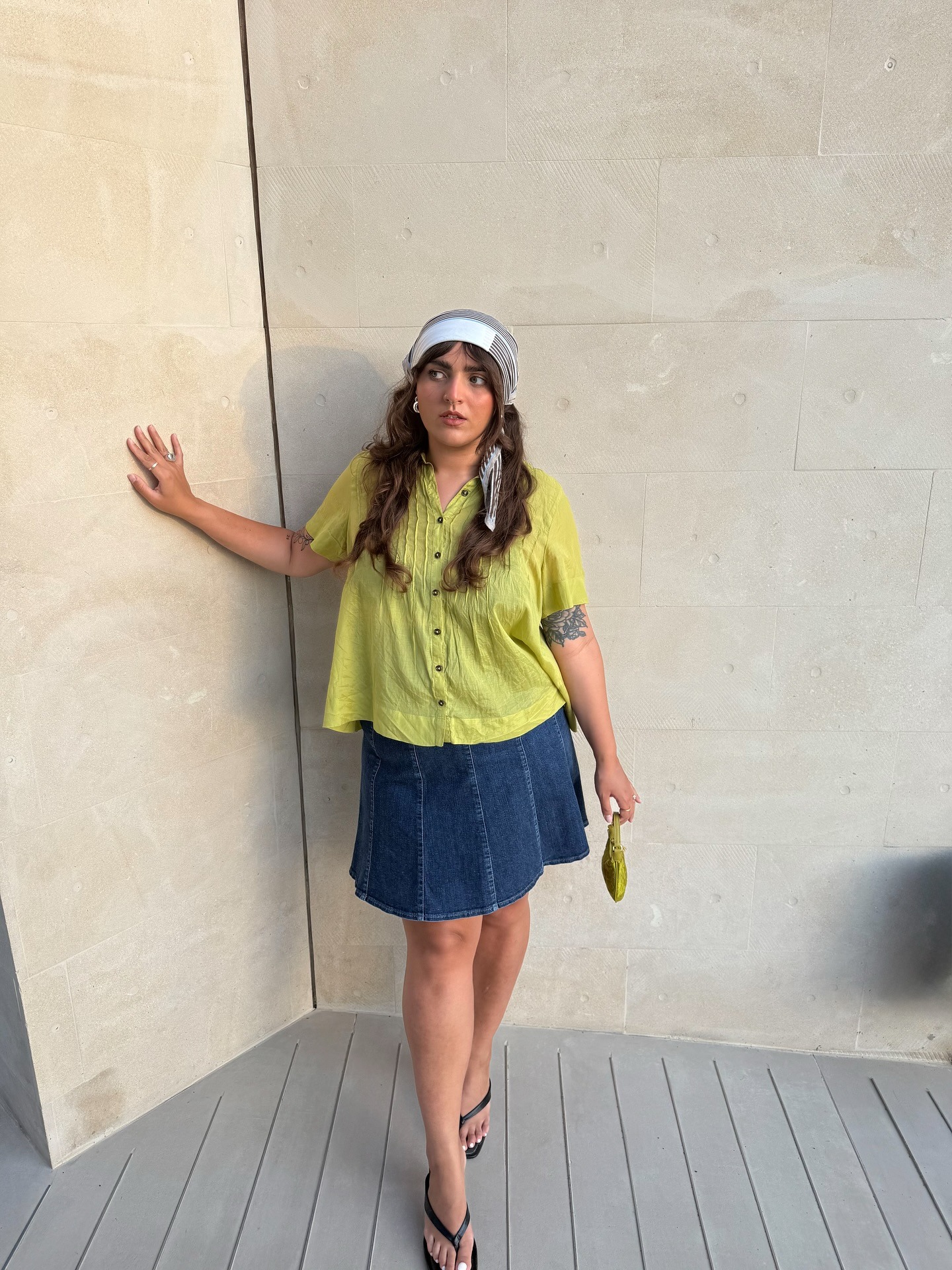 Fashion person Izabella Lilly wears a boho outfit idea. She wears a blouse with a denim midi skirt, heeled thing flip flops and a green bag. This image was taken from her Instagram recently.