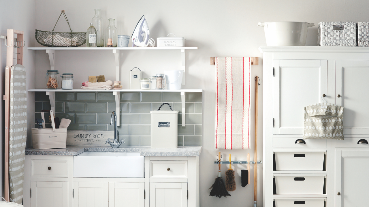 a neutral laundry room with white storage units, iron and cleaning supplies.