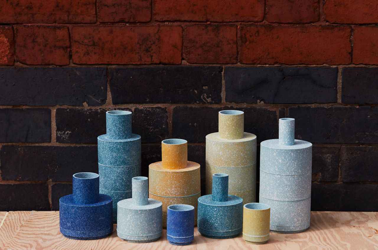 View of Granby Workshop&#039;s slip cast vessels in different shades of blue, yellow and orange on a light wood surface pictured against a dark brick wall