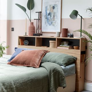 Bedroom with pink and white split painted wall, double bed, colour cushions and wooden headboard shelves