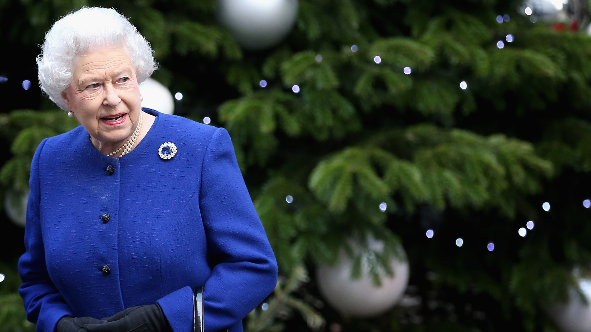Queen Elizabeth in a blue coat standing in front of a Christmas tree