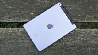 En silvrig iPad ligger utomhos på en träbänk med baksidan vänd uppåt.