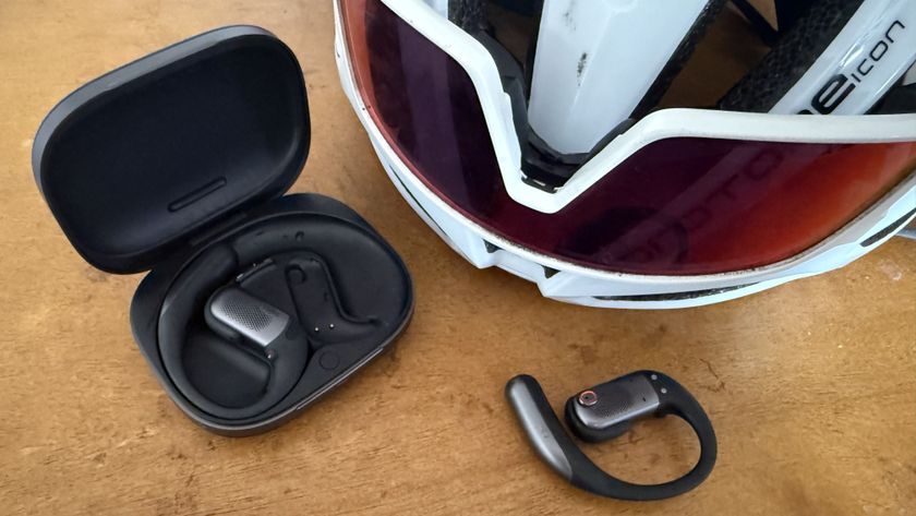 The Shokz OpenFit Pro with one of the buds outside of the case and next to a helmet and sunglasses