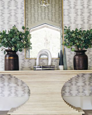 entryway with textured wallpaper, console, mirror, plants