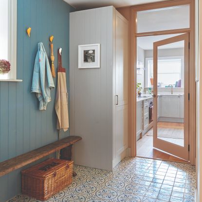 A hallway with a wall covered in wall panelling painted a fresh blue shade with yellow bird-shaped coat hooks