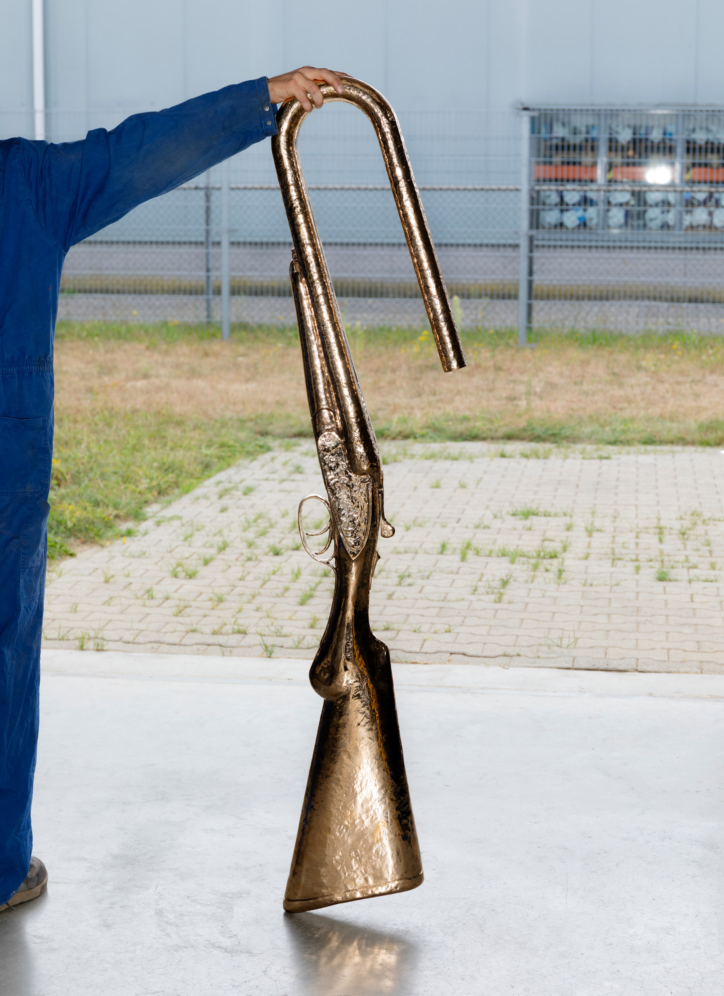 A hand holding a fake giant pistol cast in brass, inside Studio Job&#039;s Tilburg workshop