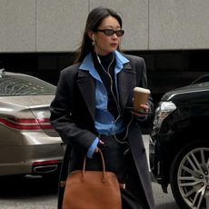 Woman wears grey coat, blue shirt, black tailored trousers