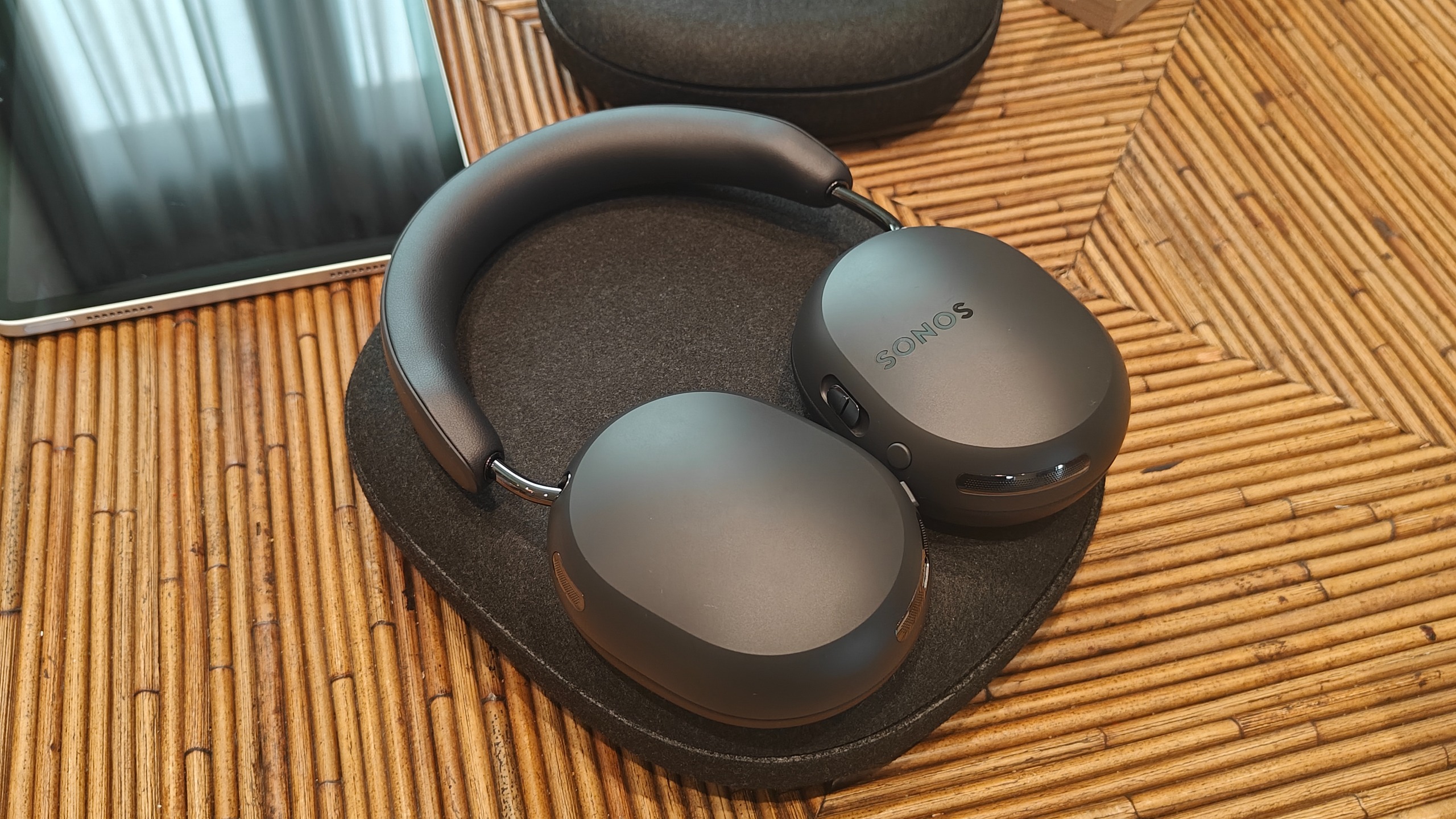 Black Ace Ultra headphones on a bamboo table surface in their case.