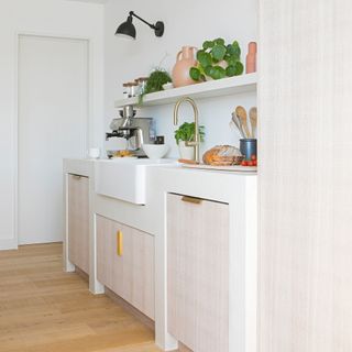 A kitchen with white butler sink, stainless steel coffee machine, brass tap and white shelving unit