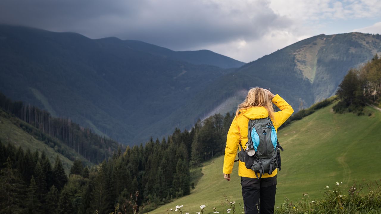 A hiker on a mountain checks out storm clouds on the horizon.