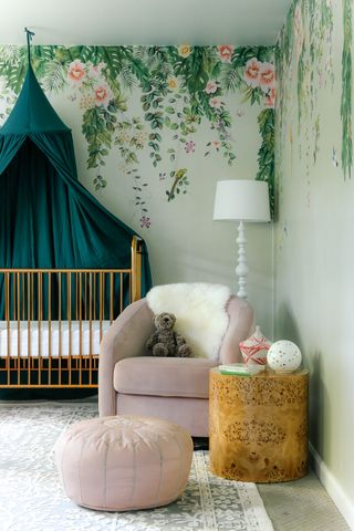 green nursery with floral mural/wallpaper, green canopy, pink armchair, white floor lamp, side table, footstool, patterned rug