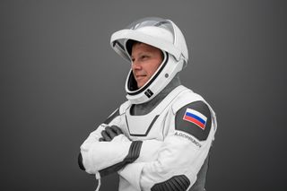 Aleksandr Gorbunov crossing his arms in a spacesuit while standing to the side of the camera