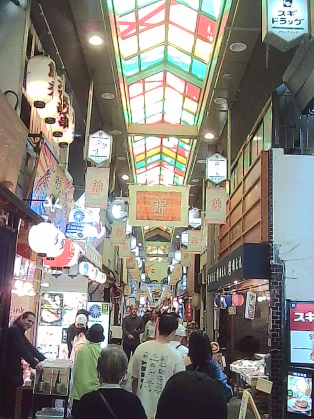 Covered shopping arcade in Japan with a colorful glass roof and glowing signs.