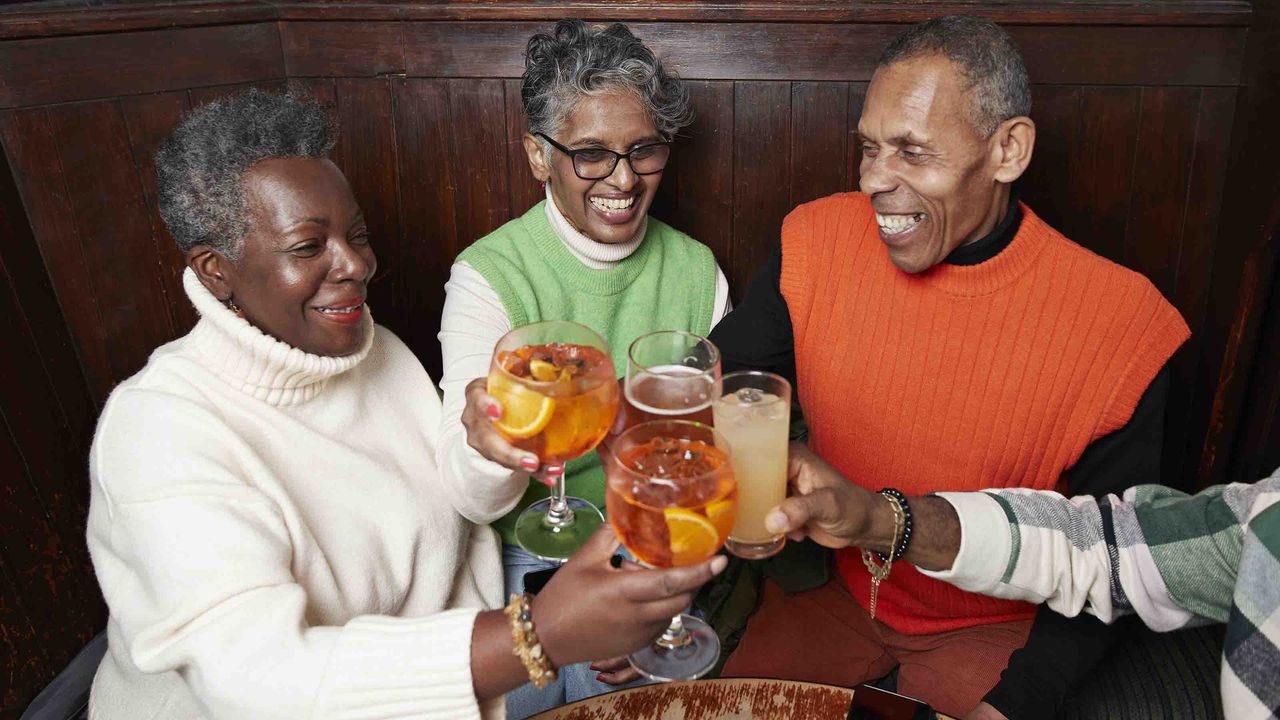 Photo of three people sitting around a table toasting each other