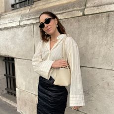 Anna LaPlaca wearing a striped button-down shirt and cream Freja shoulder bag