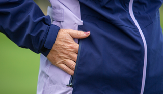 A golfer puts their hand in the pocket of the Proquip Darcey Ladies Rain Jacket