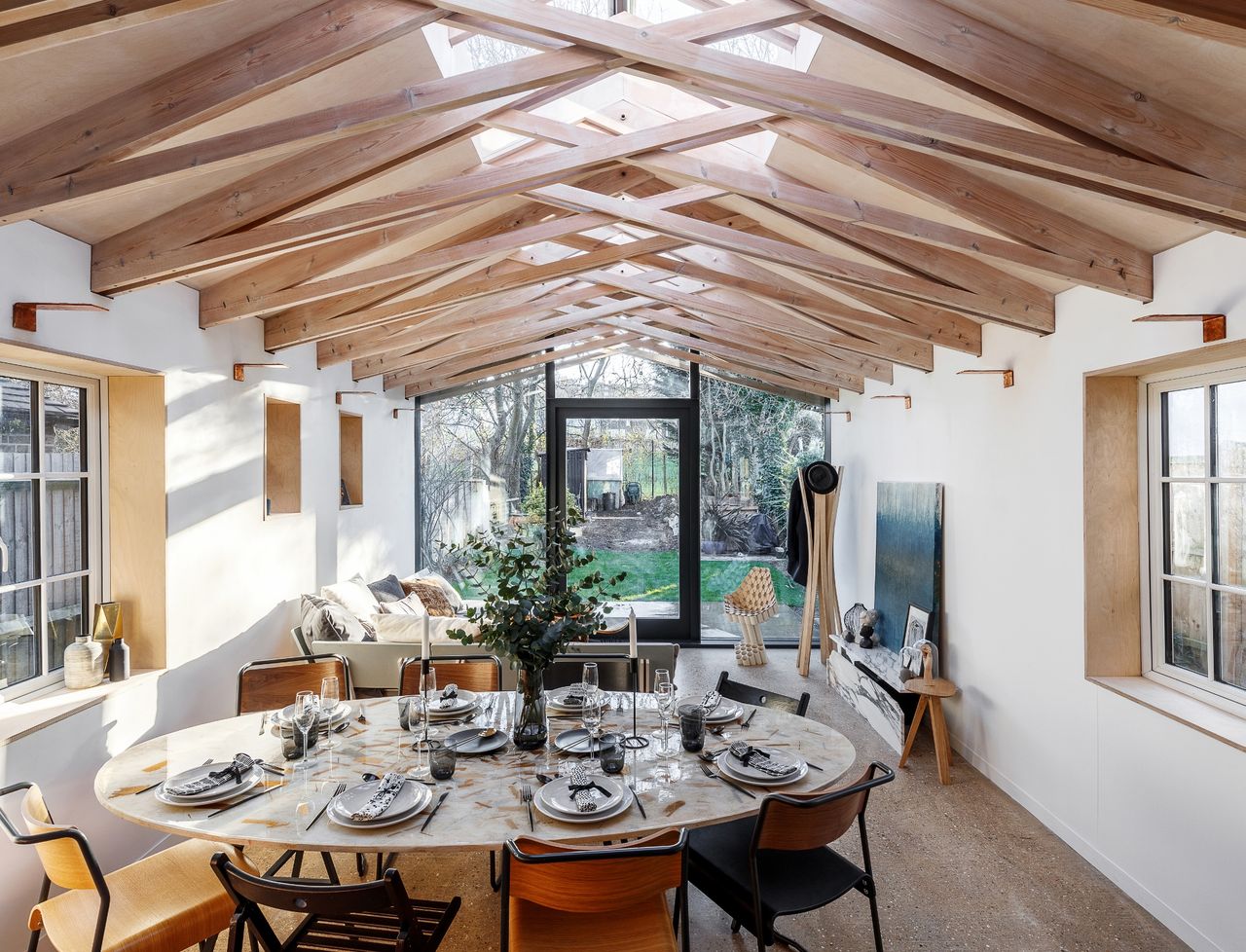 inside a single storey kitchen extension (one of the best house extensions), with wood beamed ceiling, and a large circular dining table set with plates and candles and flowers