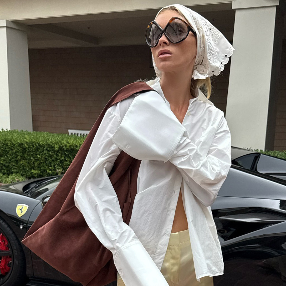 Elsa wears a white head bandana, brown suede bag, white button-down, ivory silk pants, and tan sandals.