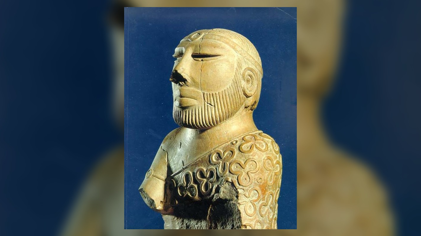 This is a bust of a priest-king. The statue is 17.5 cm high and carved from steatite a.k.a. soapstone. It was found in Mohenjo-daro in 1927. It is on display in the National Museum, Karachi, Pakistan. The statue has a beard, and is wearing a thin headpiece, as well as a cloak decorated in flowers.