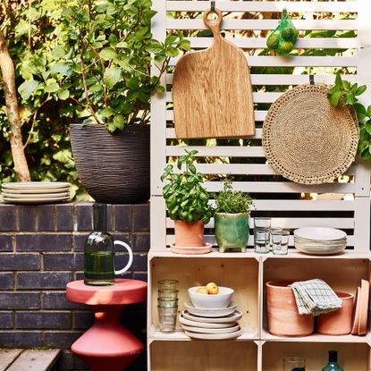 Mini outdoor kitchen set up on wooden fence panel with stacked crates