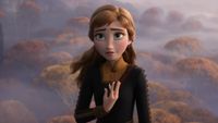 Anna from Frozen 2 stands with a concerned expression, one hand over her heart, against a misty background of autumn-colored trees.