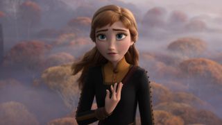 Anna from Frozen 2 stands with a concerned expression, one hand over her heart, against a misty background of autumn-colored trees.
