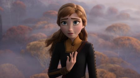 Anna from Frozen 2 stands with a concerned expression, one hand over her heart, against a misty background of autumn-colored trees.