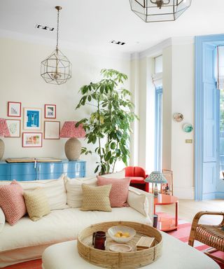 colorful living room with blue console, patterned cushions and gallery wall of colorful artwork, cream sofa and blue shutters