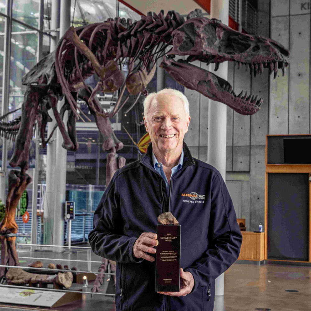 A man holds a plaque in front of a dinosaur skeleton