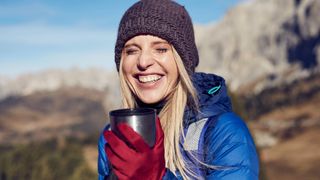 a woman holding a thermal cup with a pair of hiking gloves on