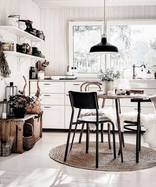 A dining idea for small kitchens with white wall paneling, wood flooring and white shelves with small round table, low-level black pendant light and jute rug