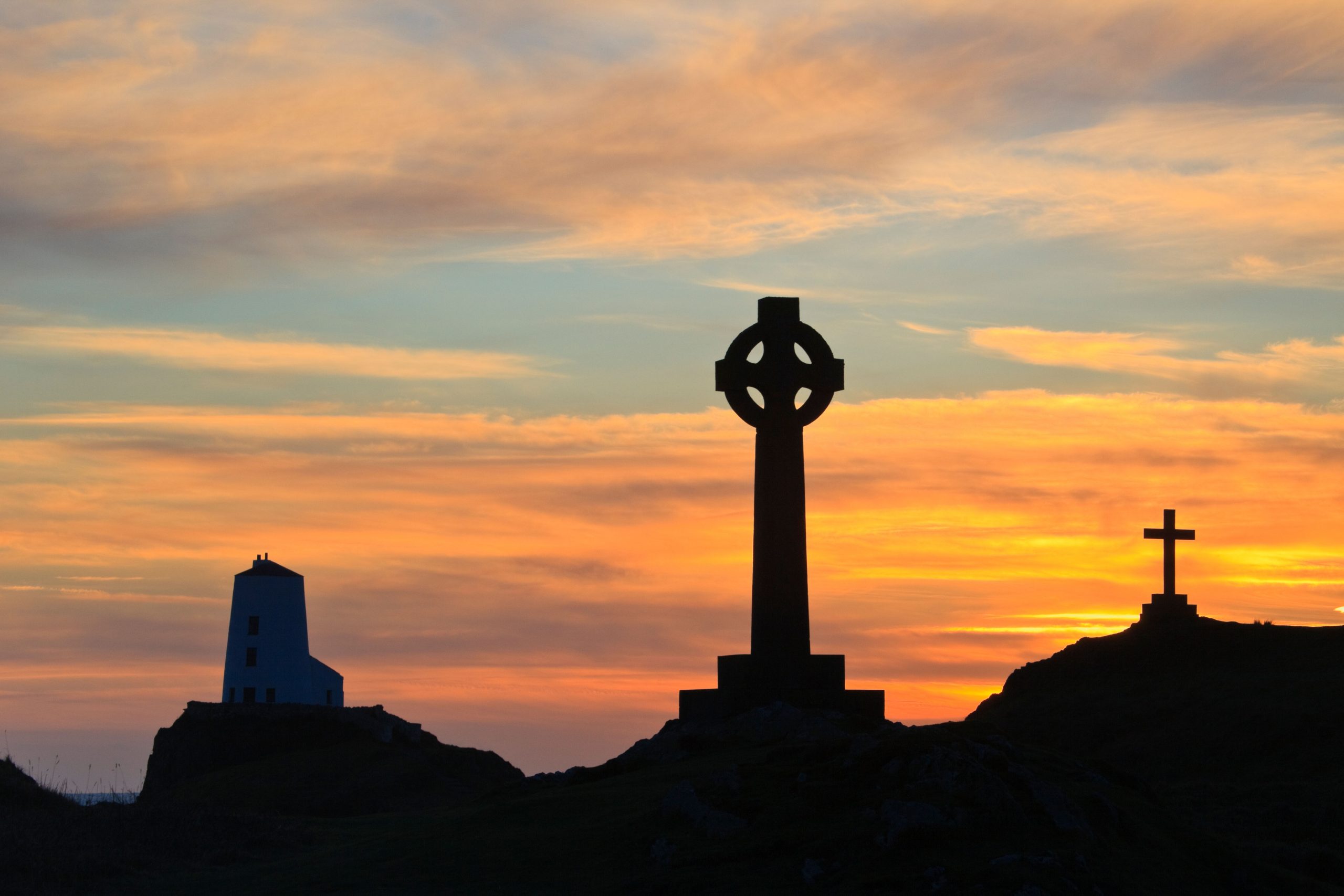St Dwynwen's Celtic cross and Twr Mawr lighthouse on Llanddwyn Island at sunset. Isle of Anglesey, North Wales.