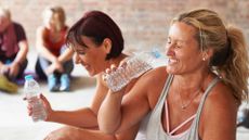 Woman laughing with others in workout room, holding a bottle of water, to represent how to control sweating
