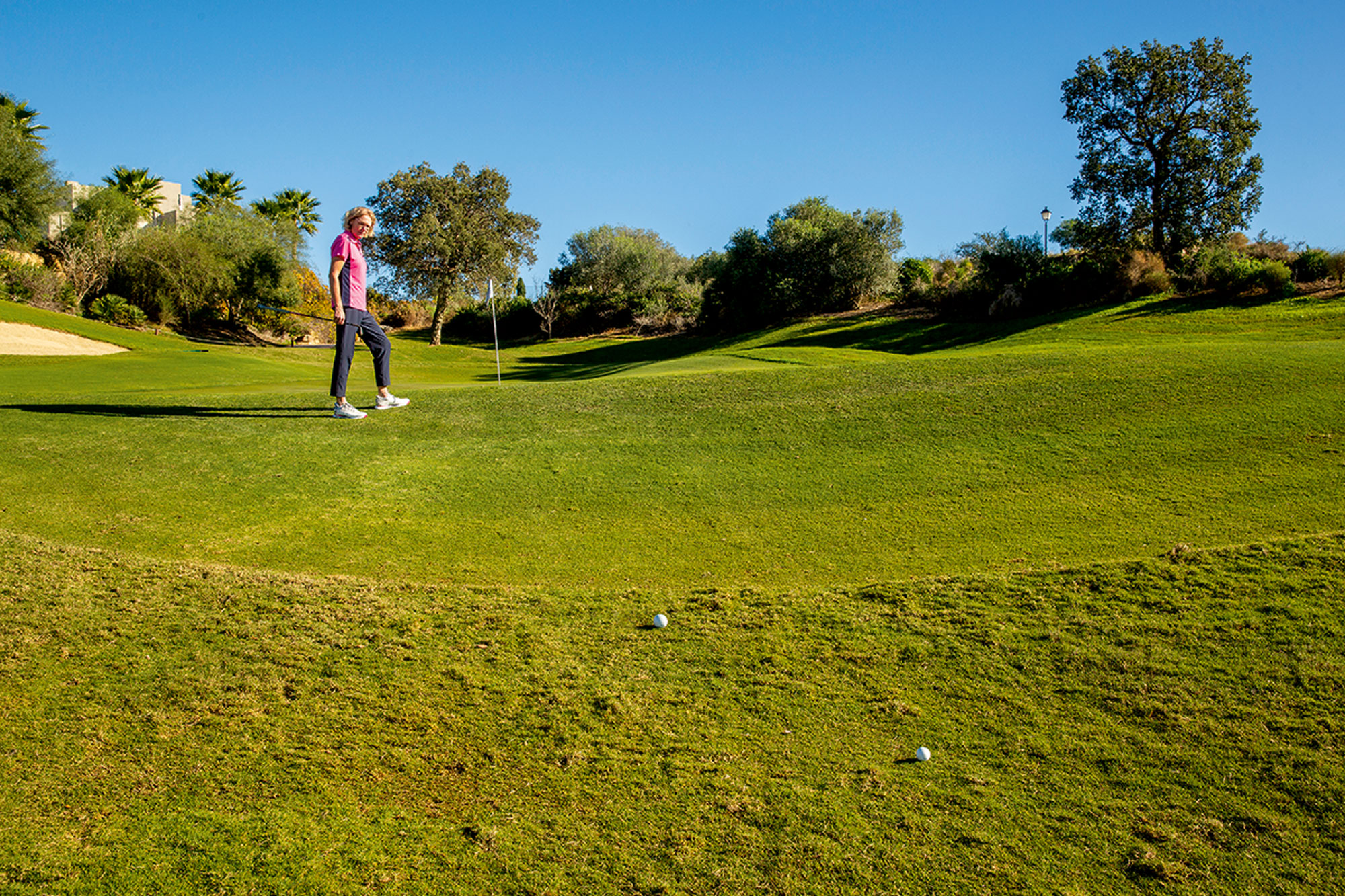 Sarah Bennett standing at the top of the raised green, looking down the hill towards her golf ball to assess distance and choose her landing spot for her chip shot