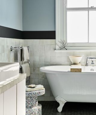 bathroom with blue wall, white tiles on lower half and white bath in front of window