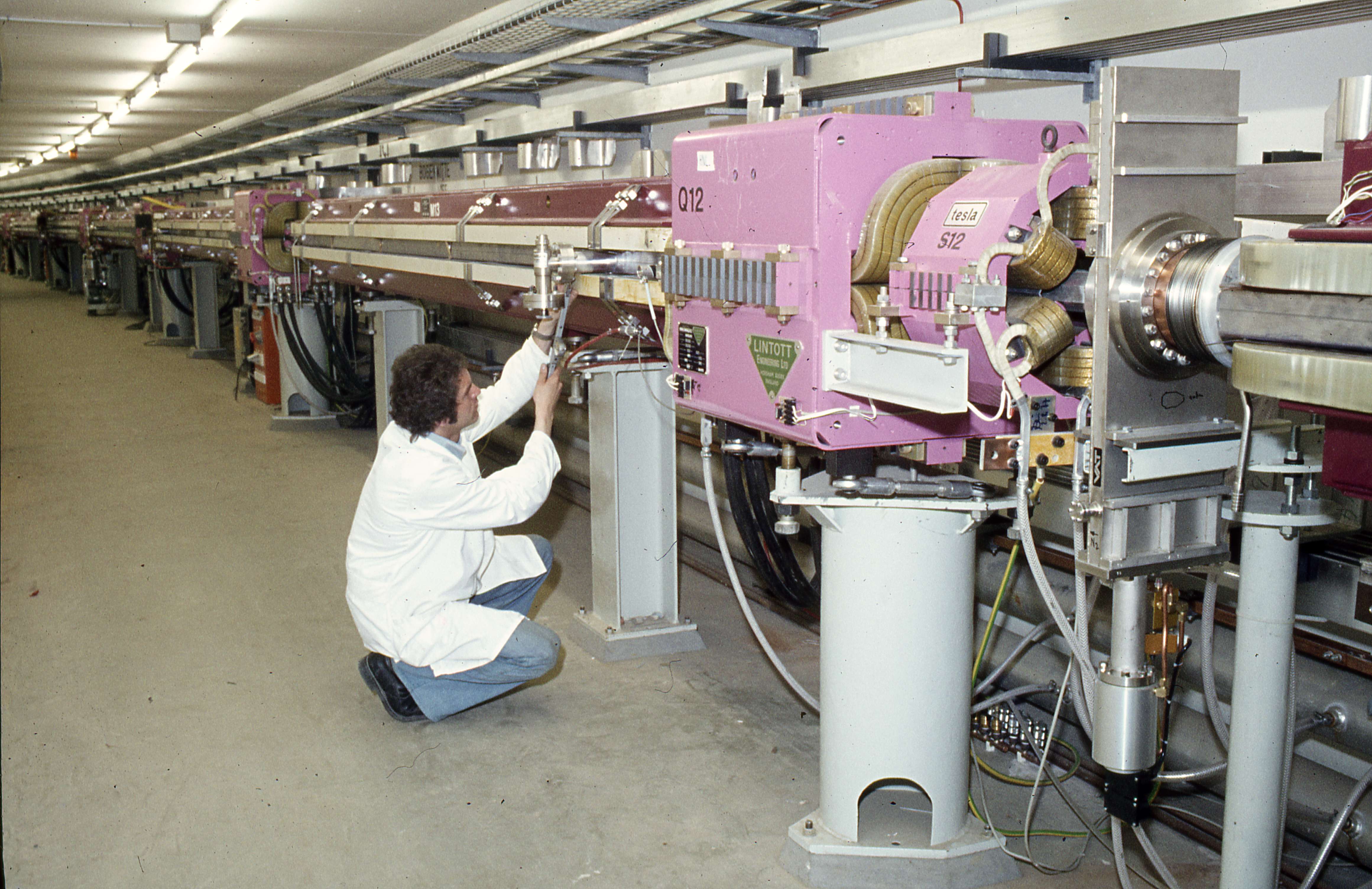 A person crouches down in a white lab coat and jeans and inspects the PETRA accelerator at DESY.