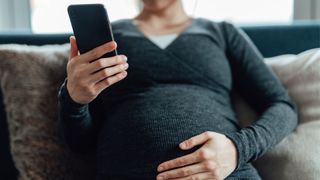 Pregnant woman holding phone with one hand and stomach with the other