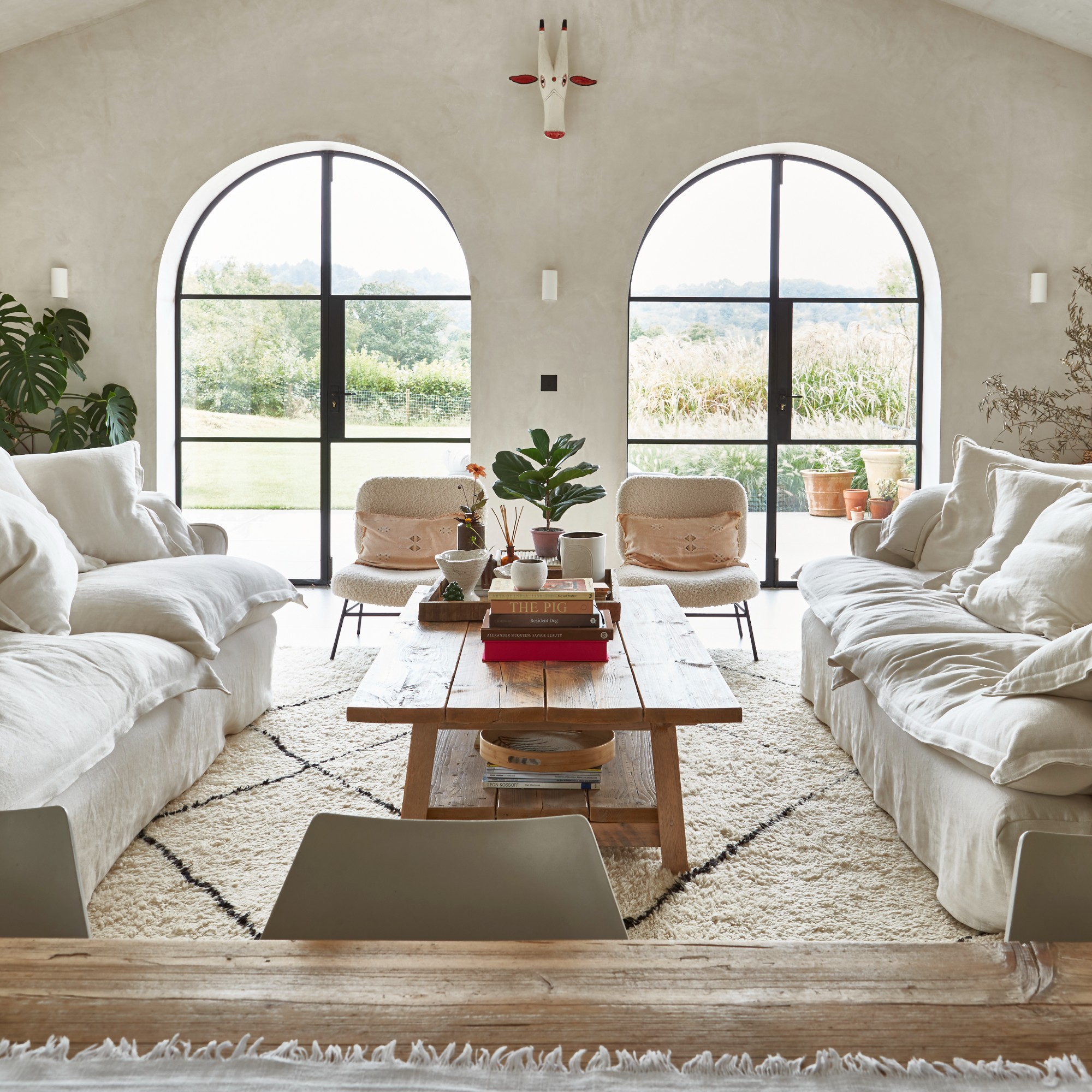 An open-plan living room with two arched windows and two white loose-cover sofas with a Berber-style rug