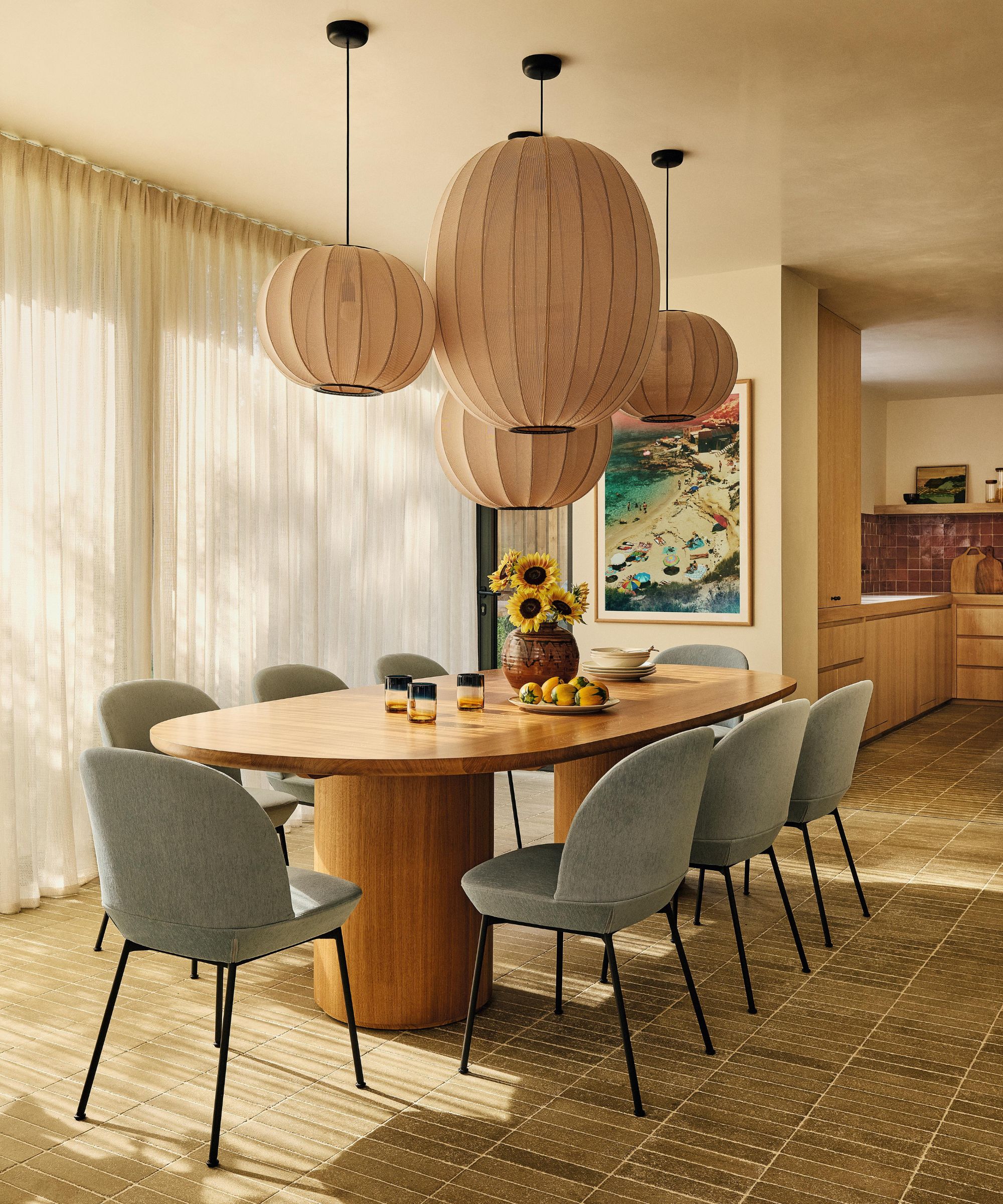 a warm neutral dining room with green floor table, wooden oak chunky table, blue dining chairs and a cluster of fabric pendants hung above the table