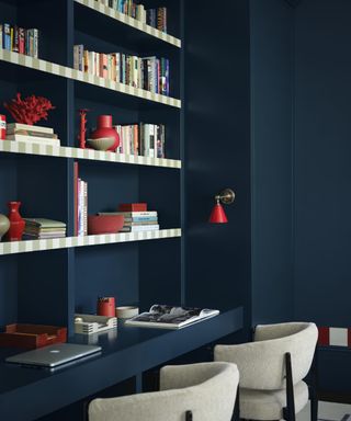 home office with dark blue color-drenched walls, shelving with books and decor, and desk space