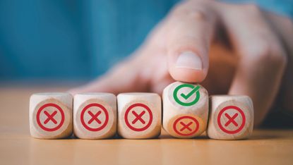 Hand flipping wooden block to change red cross mark to correct tick symbol