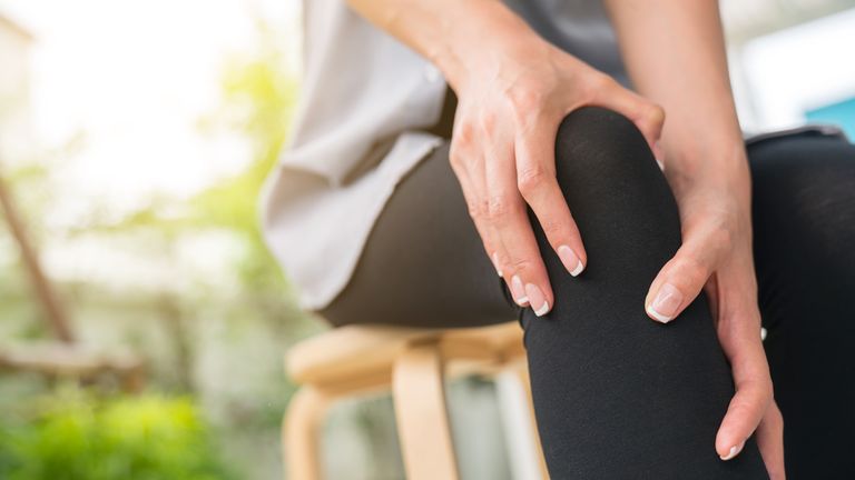 Woman suffering from joint pain clutches knee 